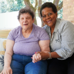 two older women smiling and sitting together, hand in hand