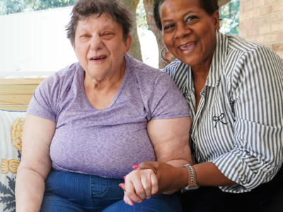 two older women smiling and sitting together, hand in hand